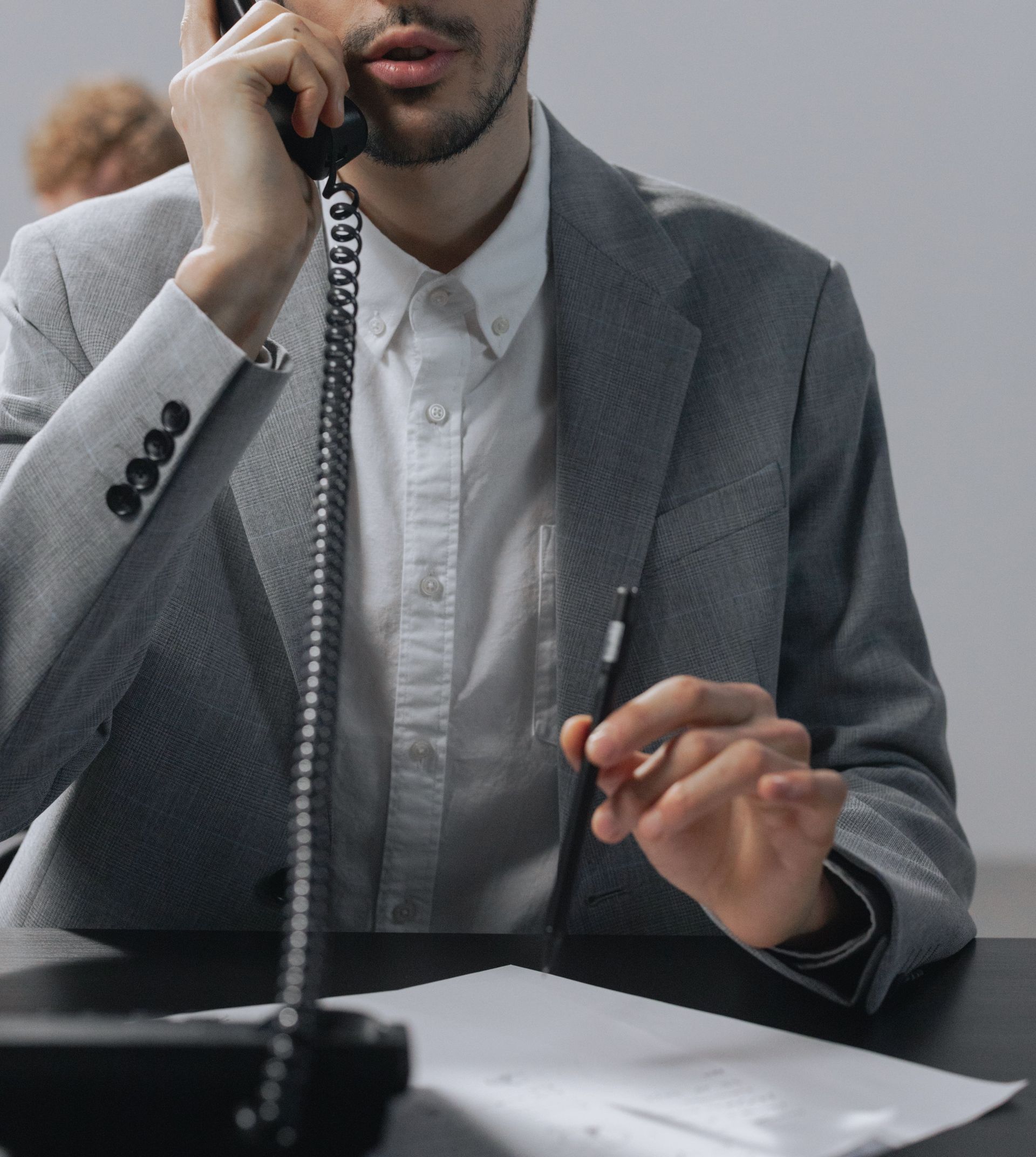 Focused young man in a gray suit conversing on telephone at an office desk.